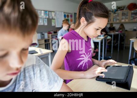 Girl sitting by boy while using digital tablet in classroom Stock Photo