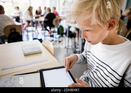 Boy using digital tablet at desk in classroom Stock Photo