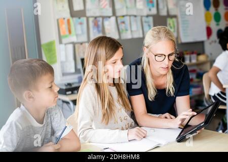 Teacher assisting students in using digital tablet at school Stock Photo