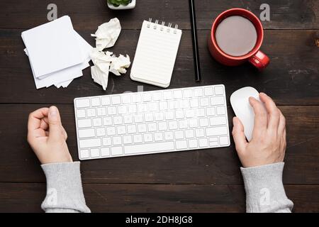 white wireless keyboard and mouse on a wooden brown table, next to a white cup with coffee, top view Stock Photo