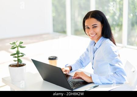 Smiling african american businesswoman sitting at her desk working on laptop Stock Photo