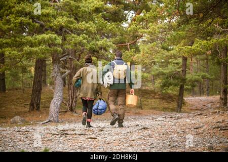 Rear view of couple carrying sleeping bags and basket in forest Stock Photo