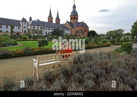Young couple sitting on a bench and enjoy the convent garden and basilica in Seligenstadt on the Banks of the River Main, Germany Stock Photo