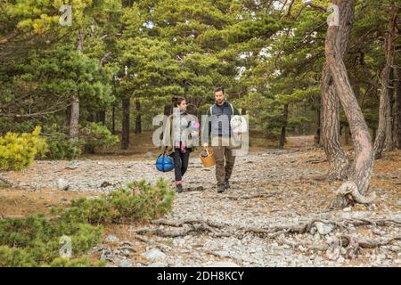Couple carrying sleeping bags and basket in forest Stock Photo