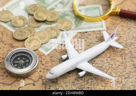 A top view closeup of a toy airplane, with coins, banknotes, compass and a magnifying glass on a map Stock Photo