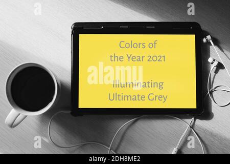 A tablet with yellow screen, earphones and a cup of tea on the grey wooden table. Colors of year 2021. Flat lay. Stock Photo