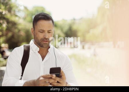 Businessman using smart phone in park during summer Stock Photo