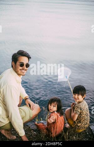 Portrait of father with daughters enjoying against lake Stock Photo