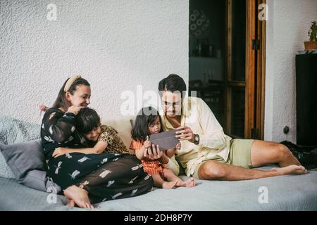 Father and disabled daughter using digital tablet while smiling girl embracing mother on sofa at home Stock Photo