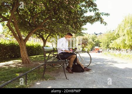 Businessman using laptop while sitting on bench at park Stock Photo