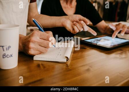 Midsection of owners working while using digital tablet in coffee shop Stock Photo