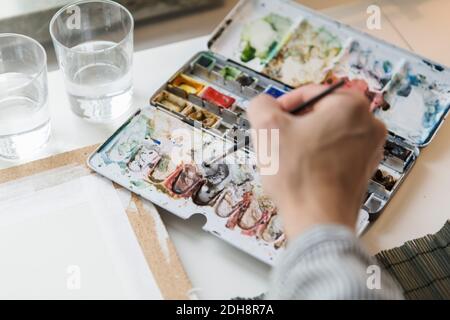 Cropped image of artist mixing watercolor paints while working in creative office