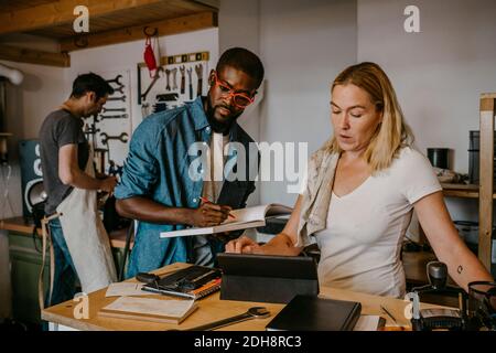 Male and female owner looking at digital tablet while colleague working in bike workshop Stock Photo