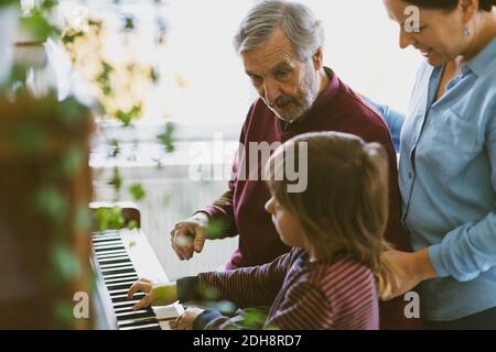 Mother and great grandfather looking at boy playing piano in house Stock Photo