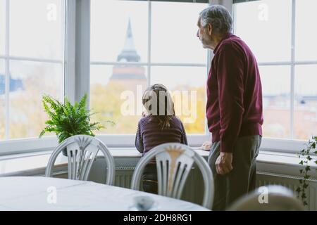 Senior man and great grandson looking through window at home Stock Photo