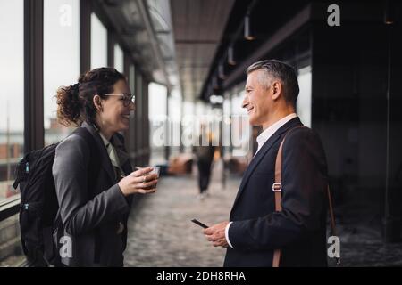 Side view of smiling business colleagues discussing while standing in corridor at workplace Stock Photo