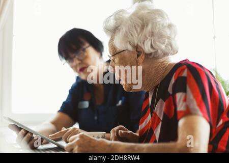 Senior woman using digital tablet with caretaker at home Stock Photo