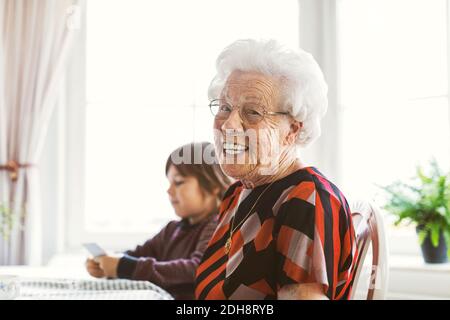 Portrait of happy senior woman sitting with great grandson playing cards at home Stock Photo