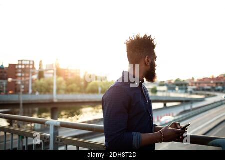 Young man with mobile phone standing on bridge against sky Stock Photo