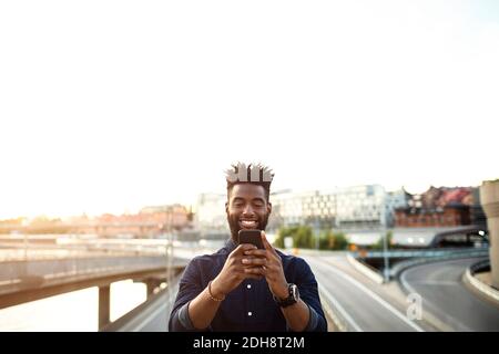 Happy man using mobile phone over city street against sky Stock Photo