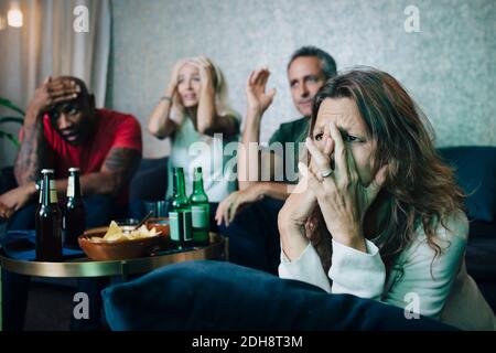 Disappointed couples watching sports in living room at night
