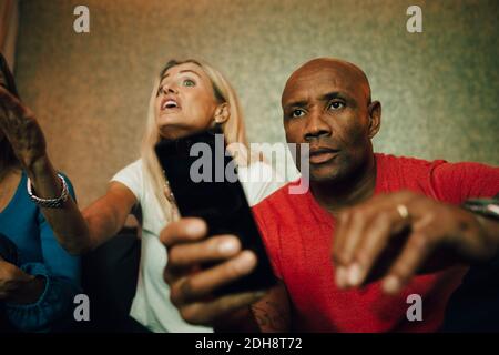 Disappointed man sitting on sofa while woman talking in background during sporting event Stock Photo