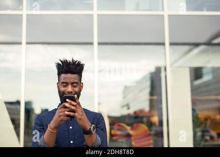 Happy young man using mobile phone against window Stock Photo