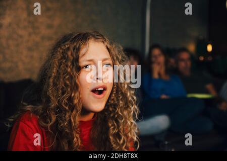 Smiling girl with family watching sports in living room at night Stock Photo