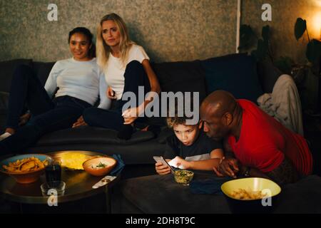 Boy using smart phone by father while mother and daughter sitting on sofa during sporting event Stock Photo