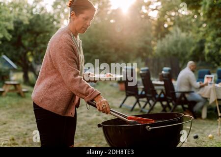 Mature woman grilling red chili pepper in yard Stock Photo