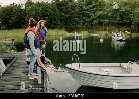 Mother preparing boat for adventure by daughters while crouching on pier during summer Stock Photo