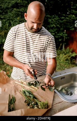 Mature man cutting plant stem while standing by sink in yard Stock Photo