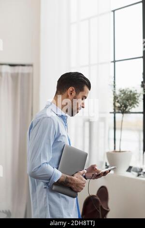 Businessman using phone while standing in office Stock Photo