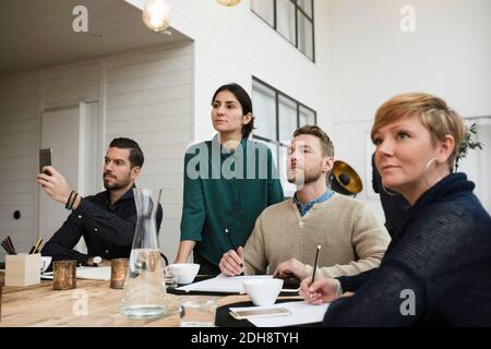 Businessman using phone while sitting by colleagues in meeting at office Stock Photo