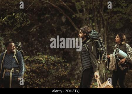 Smiling friends with backpack talking in forest during adventurous trip Stock Photo
