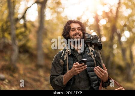 Smiling man using smart phone while looking away in forest Stock Photo