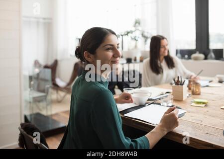 Smiling businesswoman sitting with colleagues at table in meeting Stock Photo