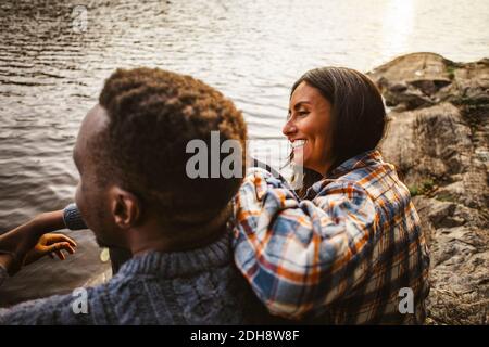 Side view of smiling woman and man sitting by lake in forest Stock Photo