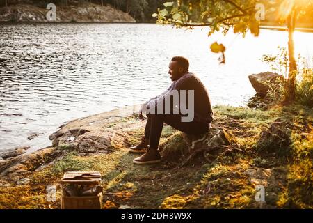 Side view of smiling man sitting by lake in forest Stock Photo