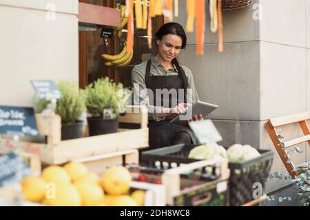 Smiling female owner using digital tablet while sitting at store entrance Stock Photo