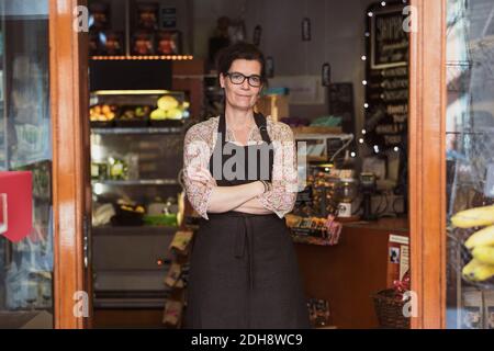 Portrait of confident owner standing with arms crossed at store seen from entrance Stock Photo