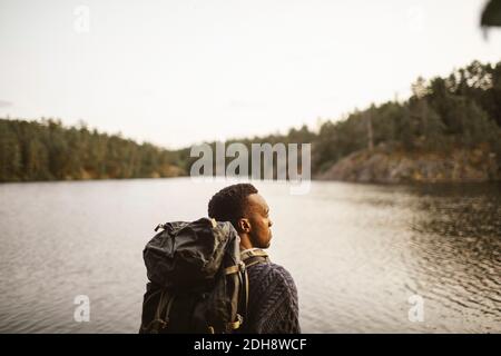 Rear view of man with backpack looking away against lake in forest Stock Photo