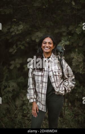 Portrait of smiling woman with hands in pockets standing in forest Stock Photo