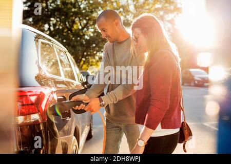 Couple charging electric car at station on sunny day Stock Photo