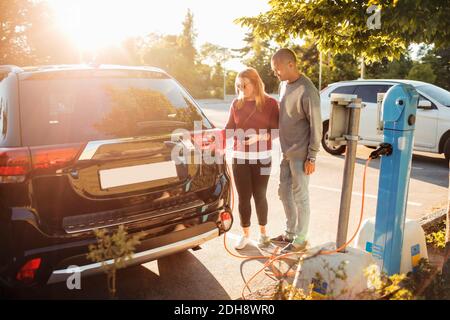 Mature couple charging electric car at station on sunny day Stock Photo