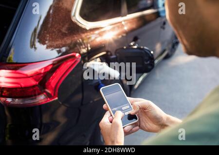 Man using mobile phone while standing by charging electric car Stock Photo