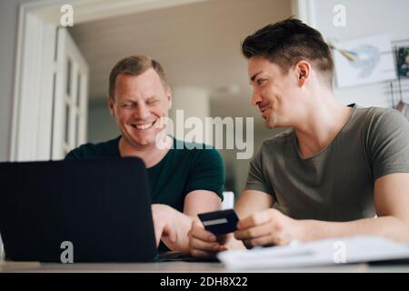 Smiling homosexual couple paying bill through laptop on dining table at home Stock Photo