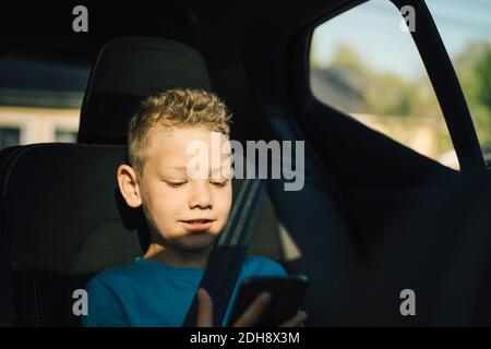 Smiling boy with seat belt using smart phone in car Stock Photo