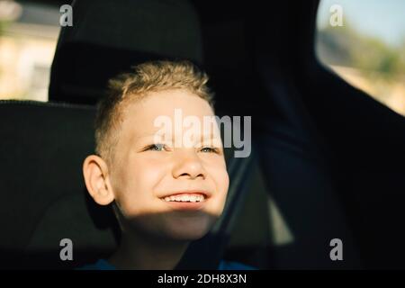 Smiling boy with seat belt looking away while sitting in car Stock Photo
