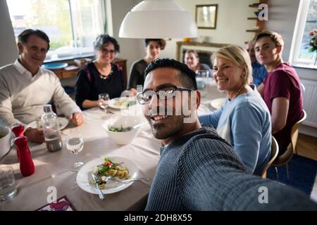 Portrait of smiling man taking selfie with family and friends at dinner party Stock Photo